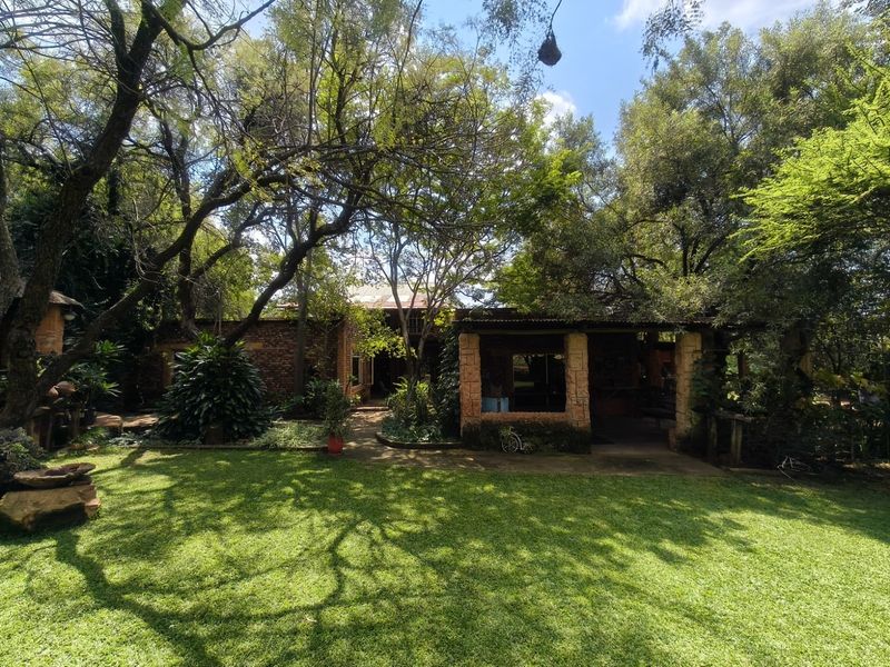 A view of the rear exterior featuring a covered patio with stone pillars, brick construction, and a well-maintained garden setting.