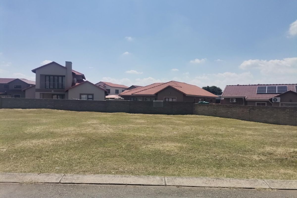 A vacant residential plot of land featuring a level grass surface, enclosed by a perimeter boundary wall in a developed suburban neighborhood.