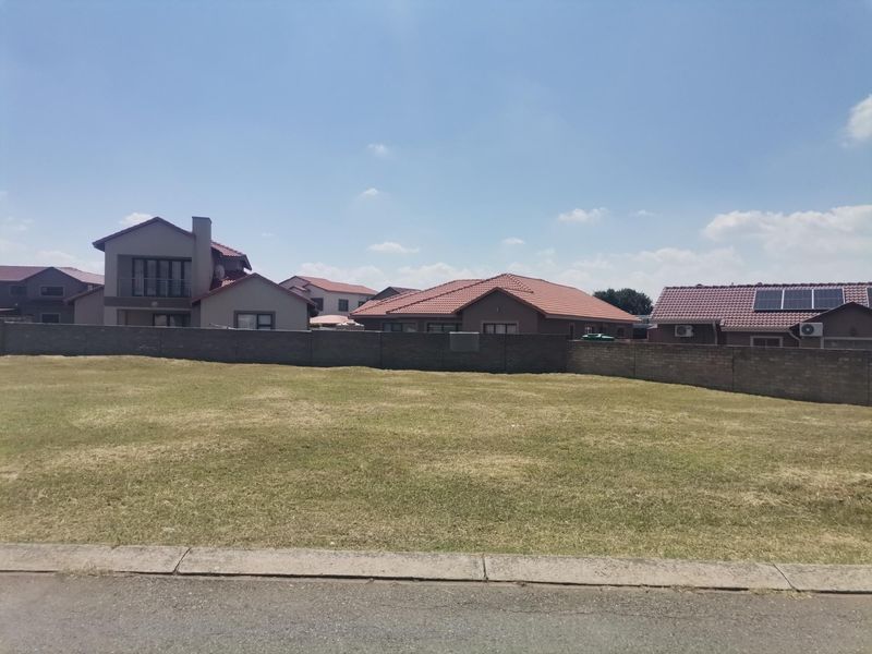 A vacant residential plot of land featuring a level grass surface, enclosed by a perimeter boundary wall in a developed suburban neighborhood.
