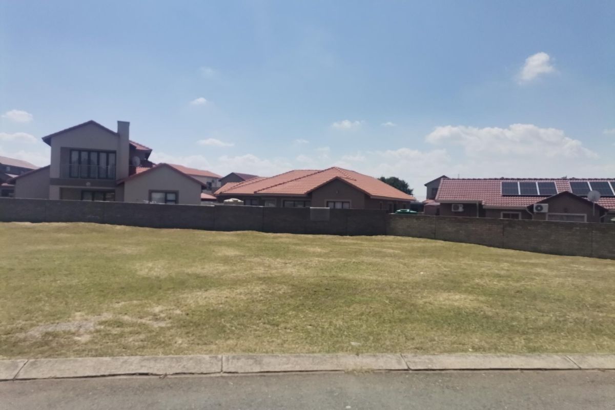 A vacant residential plot of land featuring a level grass surface and a perimeter boundary wall, situated within an established residential estate.