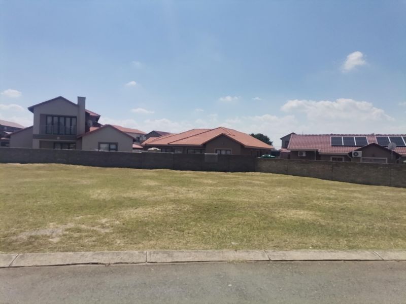 A vacant residential plot of land featuring a level grass surface and a perimeter boundary wall, situated within an established residential estate.
