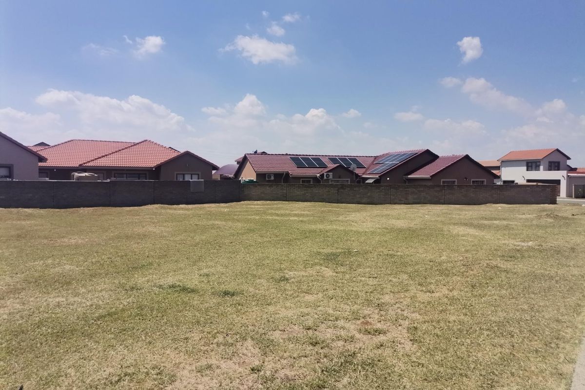 A vacant residential plot featuring a level grass lawn and a perimeter boundary wall, situated in a developed neighborhood.