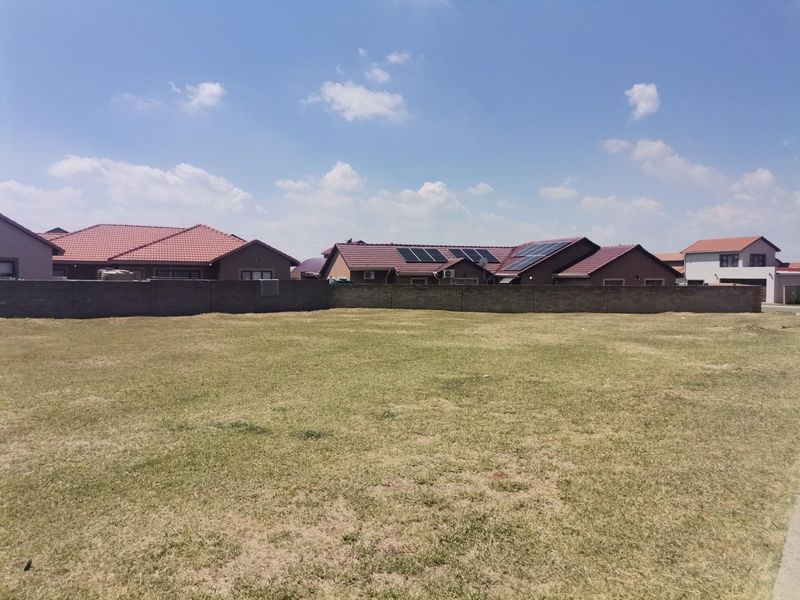 A vacant residential plot featuring a level grass lawn and a perimeter boundary wall, situated in a developed neighborhood.