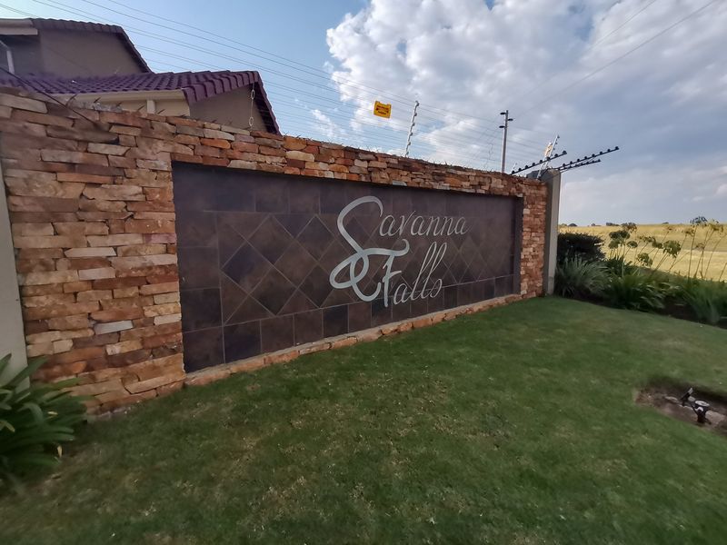 Entrance signage wall for Savanna Falls featuring stone cladding, dark tile inlay, and integrated electric security fencing.