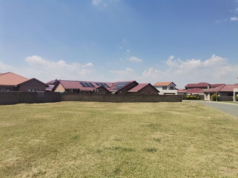 A vacant residential plot featuring a level grass lawn and a perimeter boundary wall, situated in a developed suburban neighborhood.