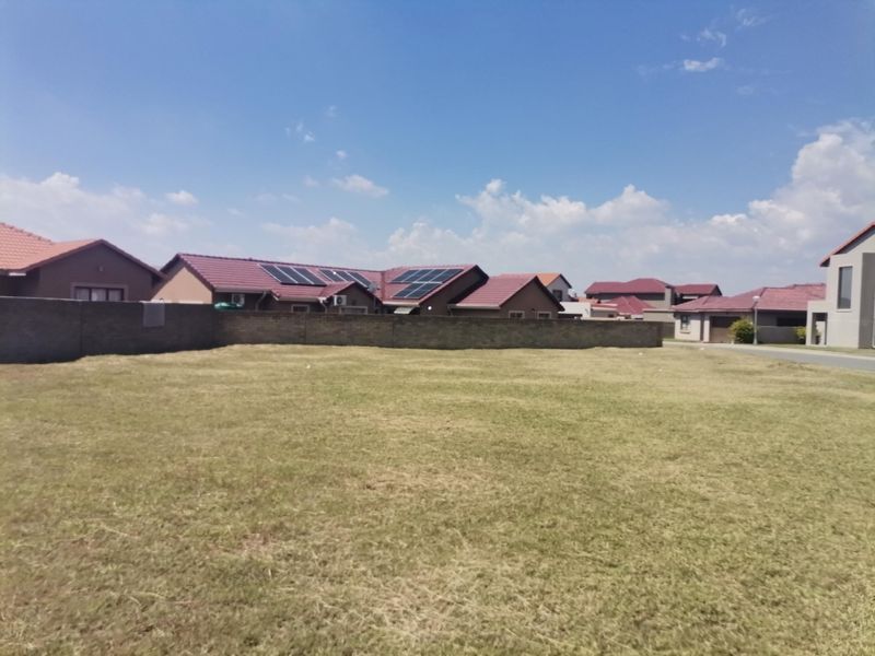 A vacant residential plot featuring a level grass lawn and a perimeter boundary wall, situated in a developed suburban neighborhood.