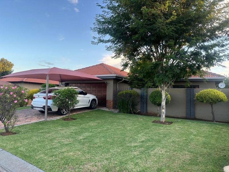 Front view of a residential property featuring a paved driveway, garage, and a well-maintained garden with a boundary wall.