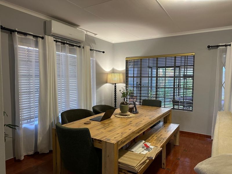 A well-lit dining area featuring tiled flooring, split-system air conditioning, and large windows with venetian blinds.