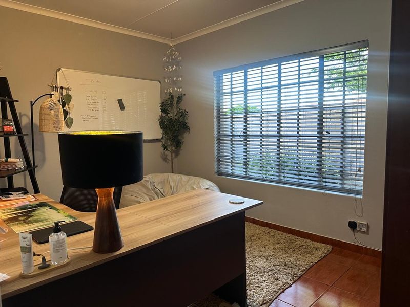 A functional home office space featuring tiled flooring, neutral wall finishes, and venetian blinds allowing natural light.