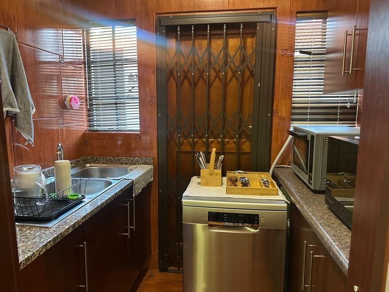 Compact scullery featuring granite countertops, double stainless steel sink, built-in cabinetry, and a secure metal gate leading to the exterior.
