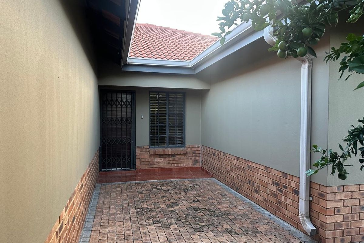 A paved rear courtyard area featuring facebrick detailing, a security gate, and a window with burglar bars, providing a functional outdoor space.