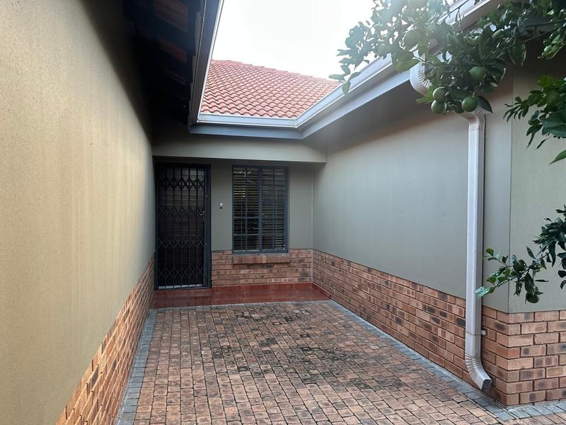 A paved rear courtyard area featuring facebrick detailing, a security gate, and a window with burglar bars, providing a functional outdoor space.