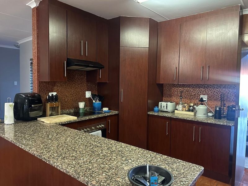 A functional kitchen featuring dark wood cabinetry, granite countertops, and a mosaic tile backsplash, providing ample storage and workspace.