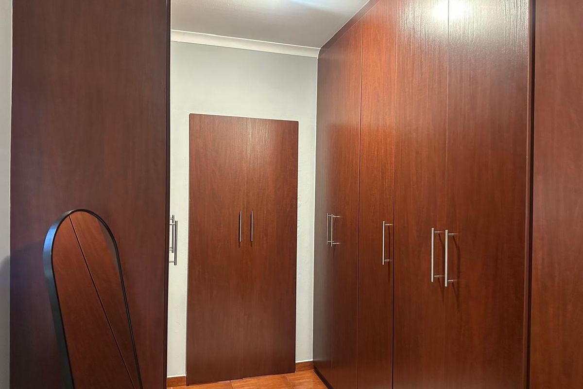 A bedroom featuring extensive dark wood built-in cupboards, tiled flooring, and a clean, neutral wall finish.