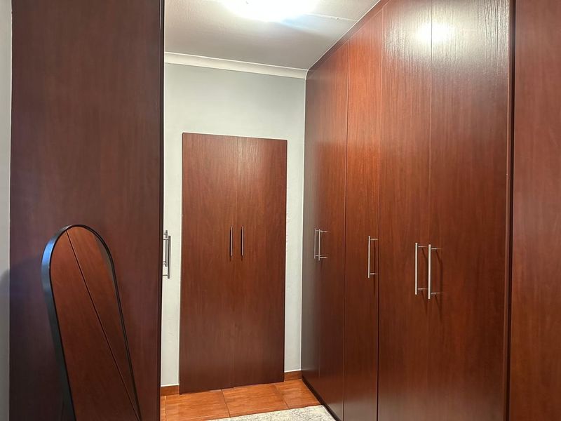 A bedroom featuring extensive dark wood built-in cupboards, tiled flooring, and a clean, neutral wall finish.