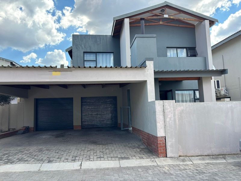 Front elevation of a modern double-storey house featuring a double garage, paved driveway, and covered carport area with contemporary grey facade finishes.