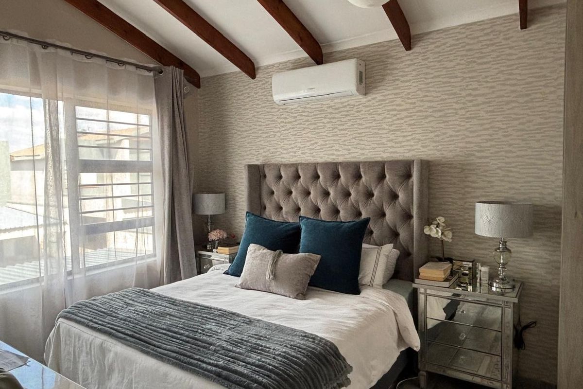A well-maintained bedroom featuring exposed timber ceiling beams, textured wallpaper, and a wall-mounted split-system air conditioning unit.