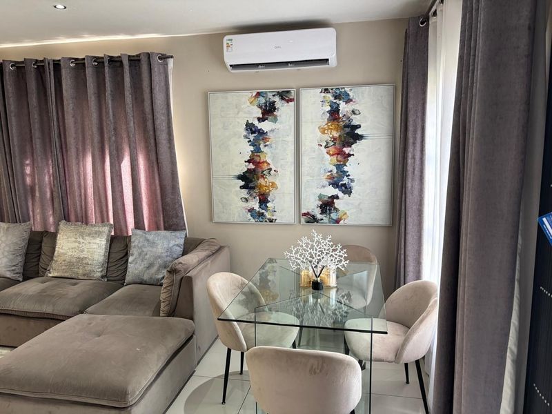 A well-maintained open-plan living and dining area featuring tiled flooring, recessed downlighting, and a wall-mounted split-system air conditioning unit.