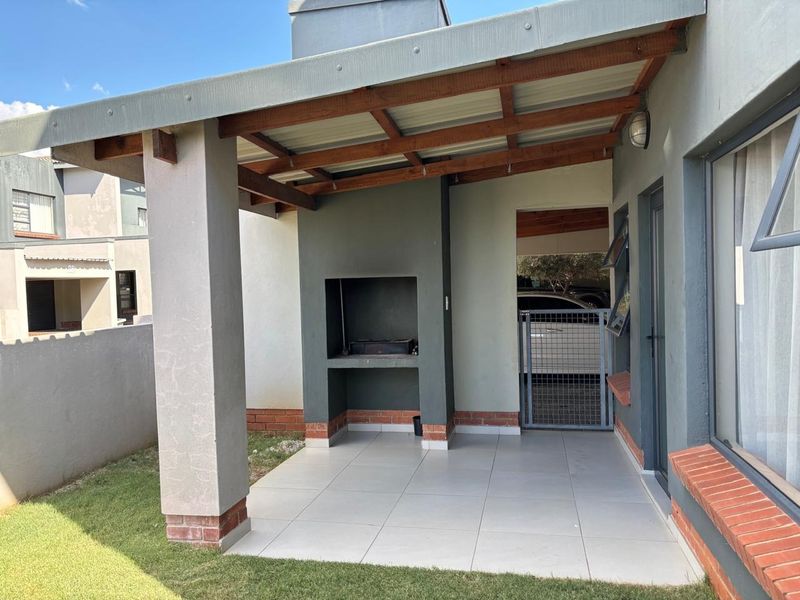 Covered patio area featuring a built-in braai, tiled flooring, and a timber-framed roof structure, providing a functional outdoor entertainment space.