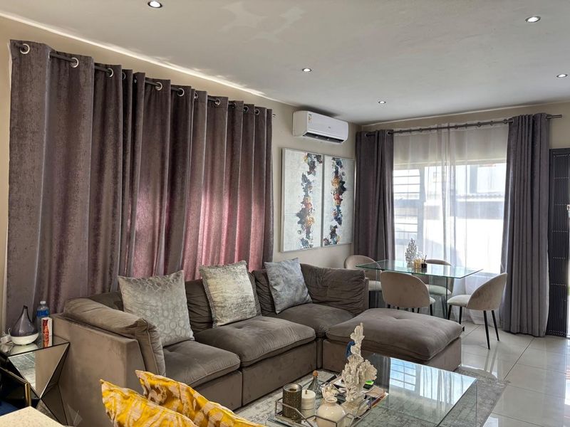 A well-maintained living room featuring tiled flooring, recessed downlighting, and a wall-mounted air conditioning unit, creating a comfortable and functional living space.