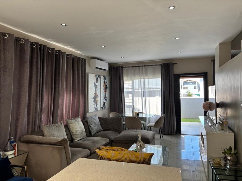 Open-plan living area featuring tiled flooring, recessed downlighting, a wall-mounted air conditioning unit, and direct access to the outdoor patio through a sliding glass door.