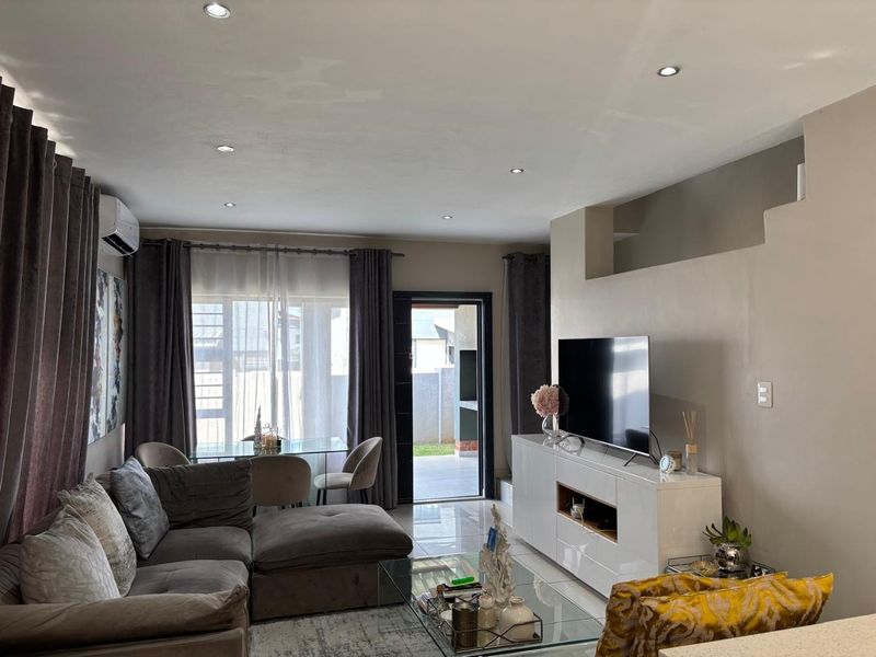 A well-lit living room featuring tiled flooring, recessed downlighting, and a split-system air conditioner, with direct access to an outdoor patio area.