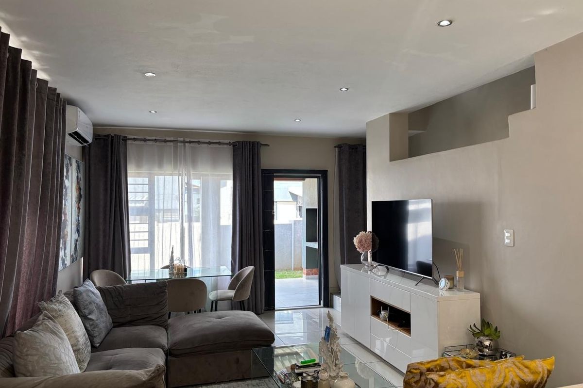 A well-lit living room featuring tiled flooring, recessed downlighting, and a split-system air conditioner, with direct access to an outdoor patio area.
