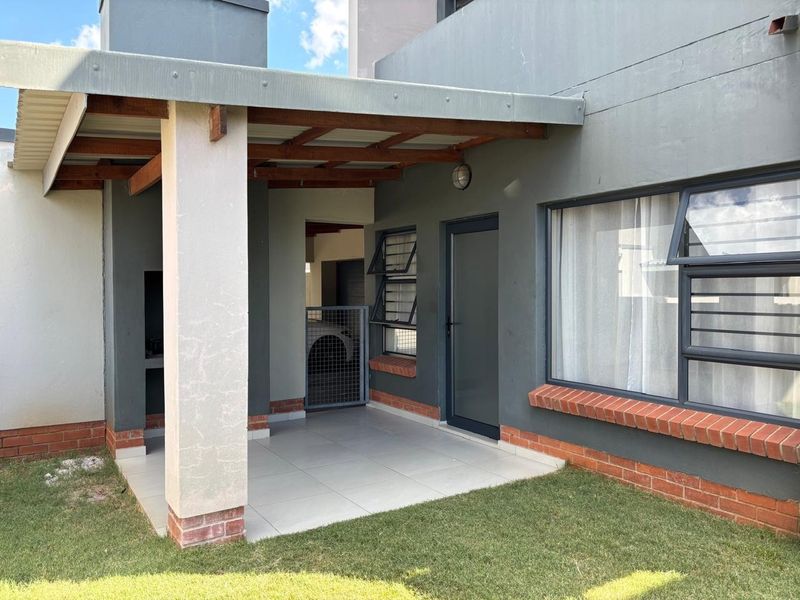 A covered patio area featuring tiled flooring, a built-in braai, and a timber pergola, providing a functional outdoor entertainment space.