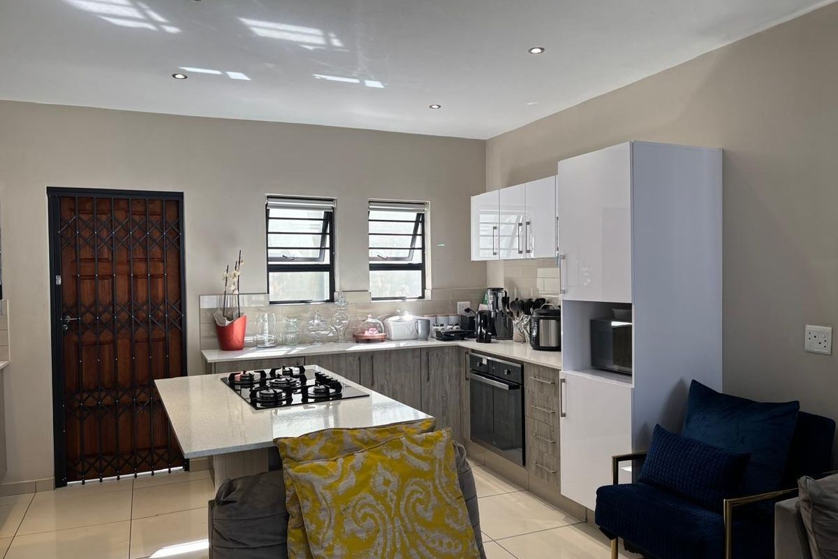 Modern kitchen featuring a central island with a gas hob, built-in oven, sleek cabinetry, quartz countertops, and tiled flooring.