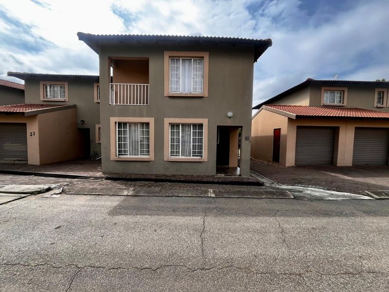 Front elevation of a two-story townhouse featuring a tiled roof, balcony with railing, and paved driveway access.