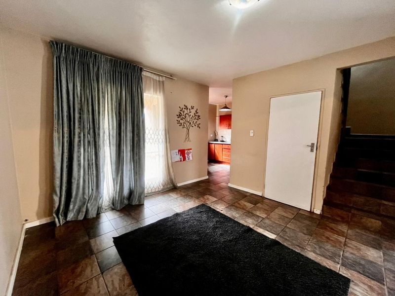 Open plan living area featuring tiled flooring, a sliding door with security gate, and access to the kitchen and staircase.