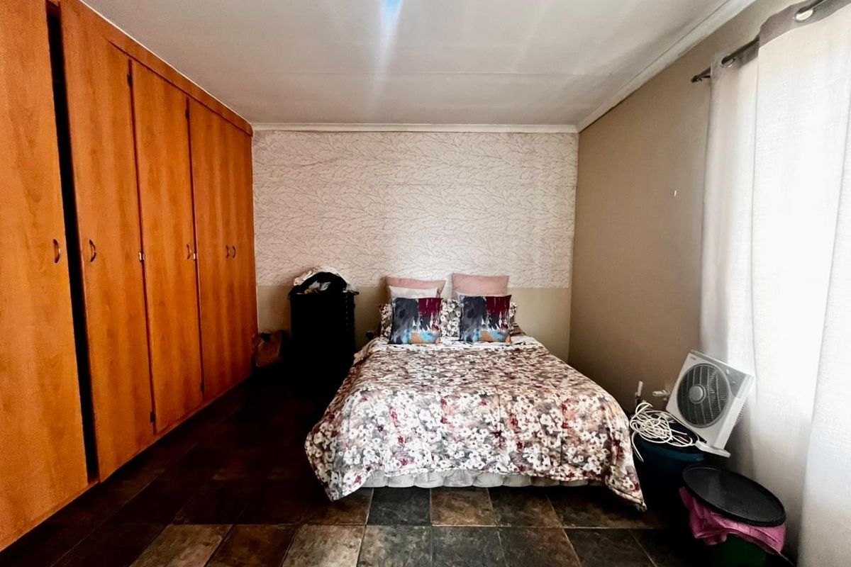 A bedroom featuring built-in wooden cupboards, tiled flooring, and a feature wall, offering a functional space with potential for modern updates.
