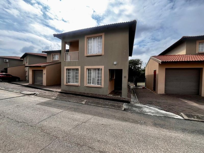 Front exterior view of a two-story townhouse featuring a tiled roof, paved driveway, and a small upper-level balcony.