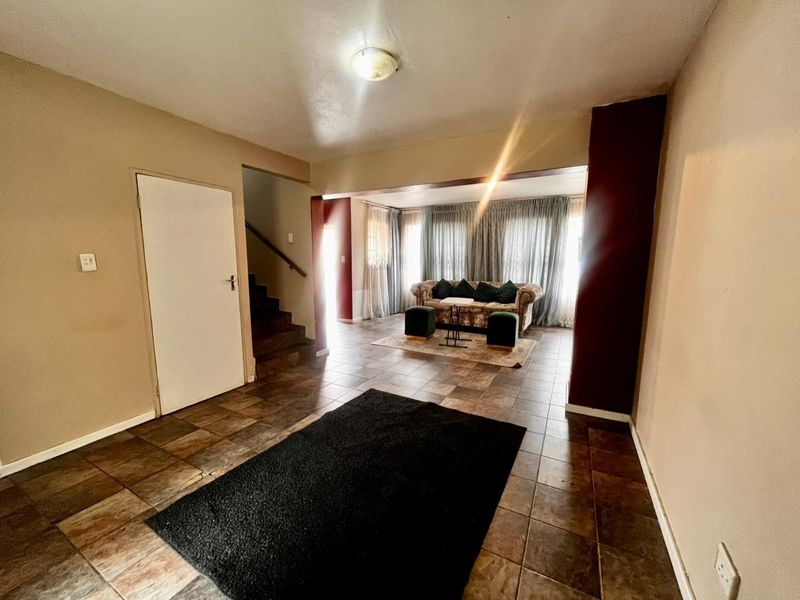 Spacious living area featuring tiled flooring and an internal staircase, offering a functional layout with potential for modern updates.
