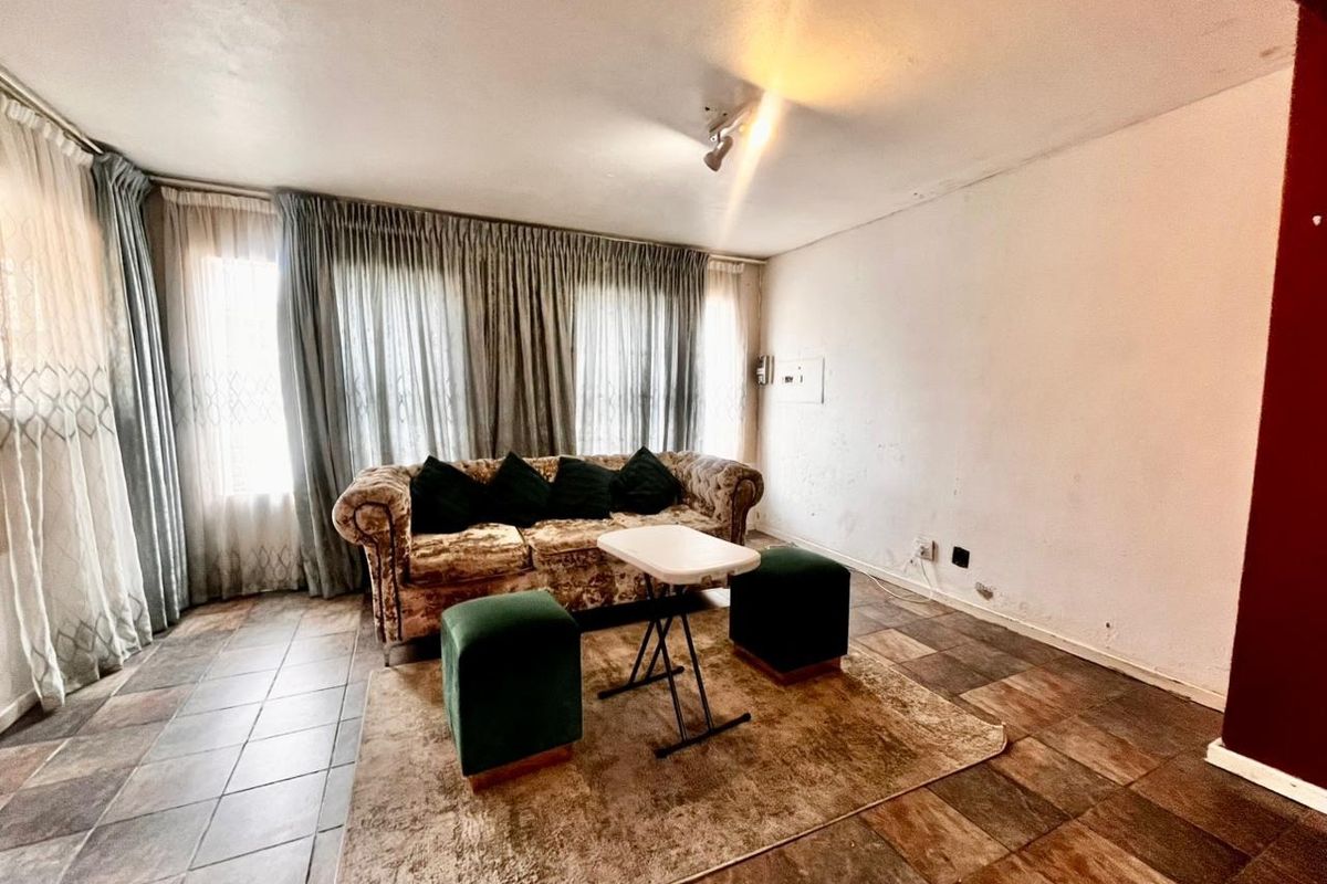 A living room area featuring tiled flooring and large windows with curtain tracks, requiring cosmetic updates to the walls and flooring.