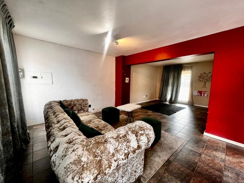 Open plan living area featuring tiled flooring and a distinct red accent wall, providing a versatile space for lounge and dining arrangements.
