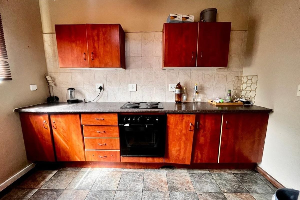 A functional kitchen featuring wooden cabinetry, a built-in oven and hob, tiled splashback, and durable tiled flooring, offering potential for modern cosmetic updates.
