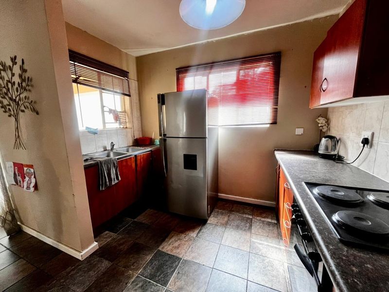 A functional kitchen featuring built-in cabinetry, laminate countertops, a stainless steel sink, and an electric hob with tiled flooring.