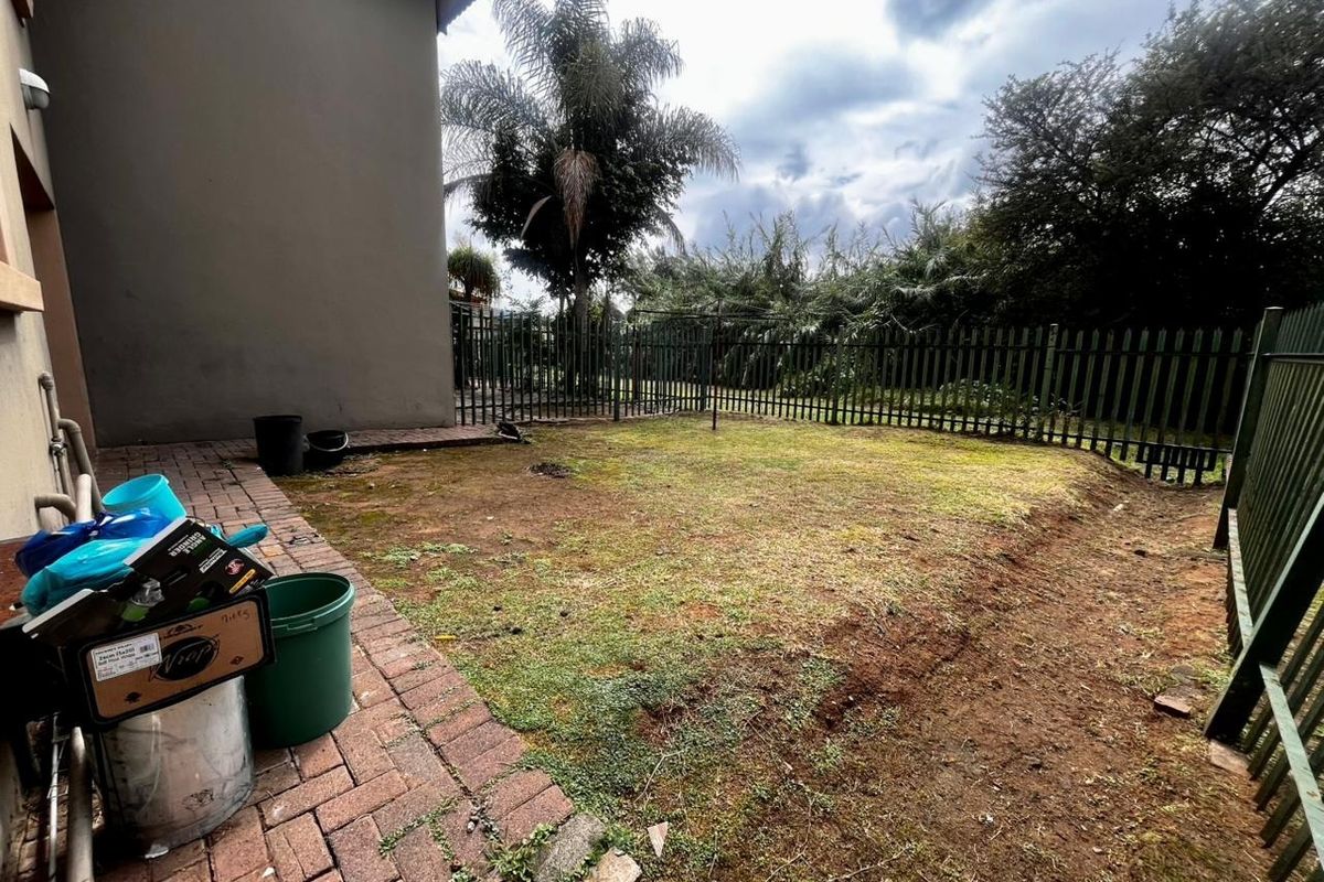 Rear garden area featuring a paved walkway, metal perimeter fencing, and a lawn area in need of maintenance.