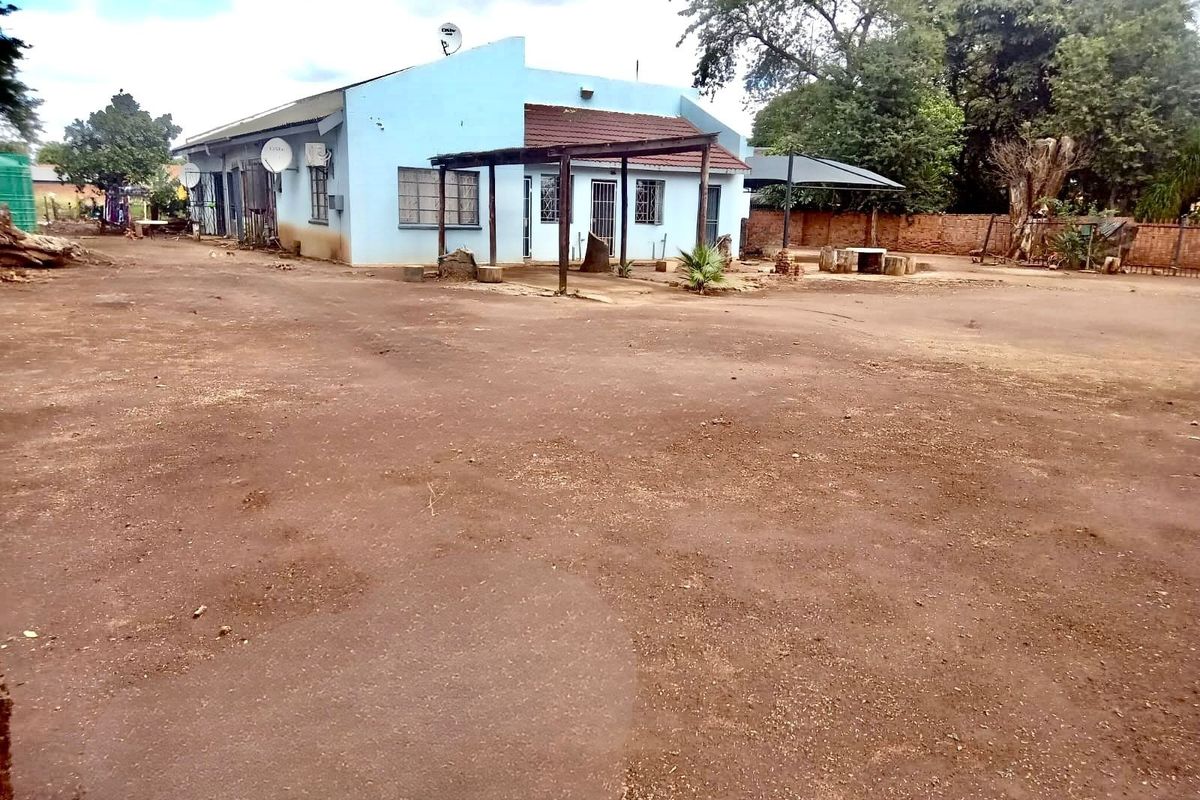 Rear view of a single-story house featuring a covered patio area and a large, unpaved yard space.