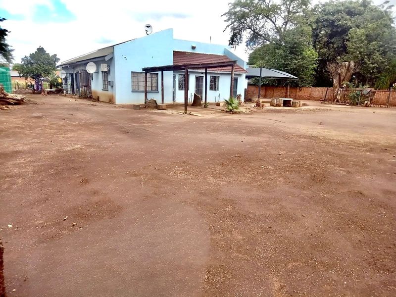 Rear view of a single-story house featuring a covered patio area and a large, unpaved yard space.
