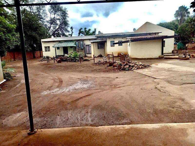 Rear view of the property showing a large unpaved yard, concrete driveway, and the rear building elevation with a covered patio area.