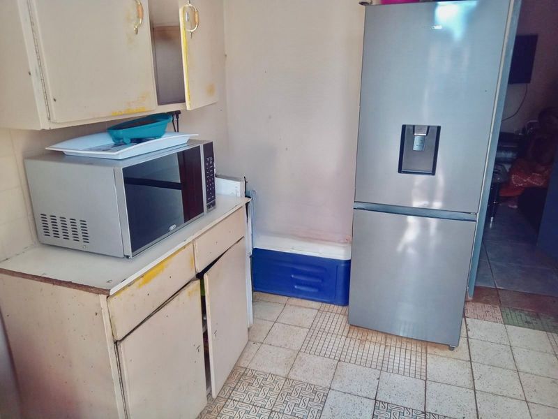 A small kitchen area featuring dated built-in cabinetry and tiled flooring, currently showing significant signs of wear and tear.