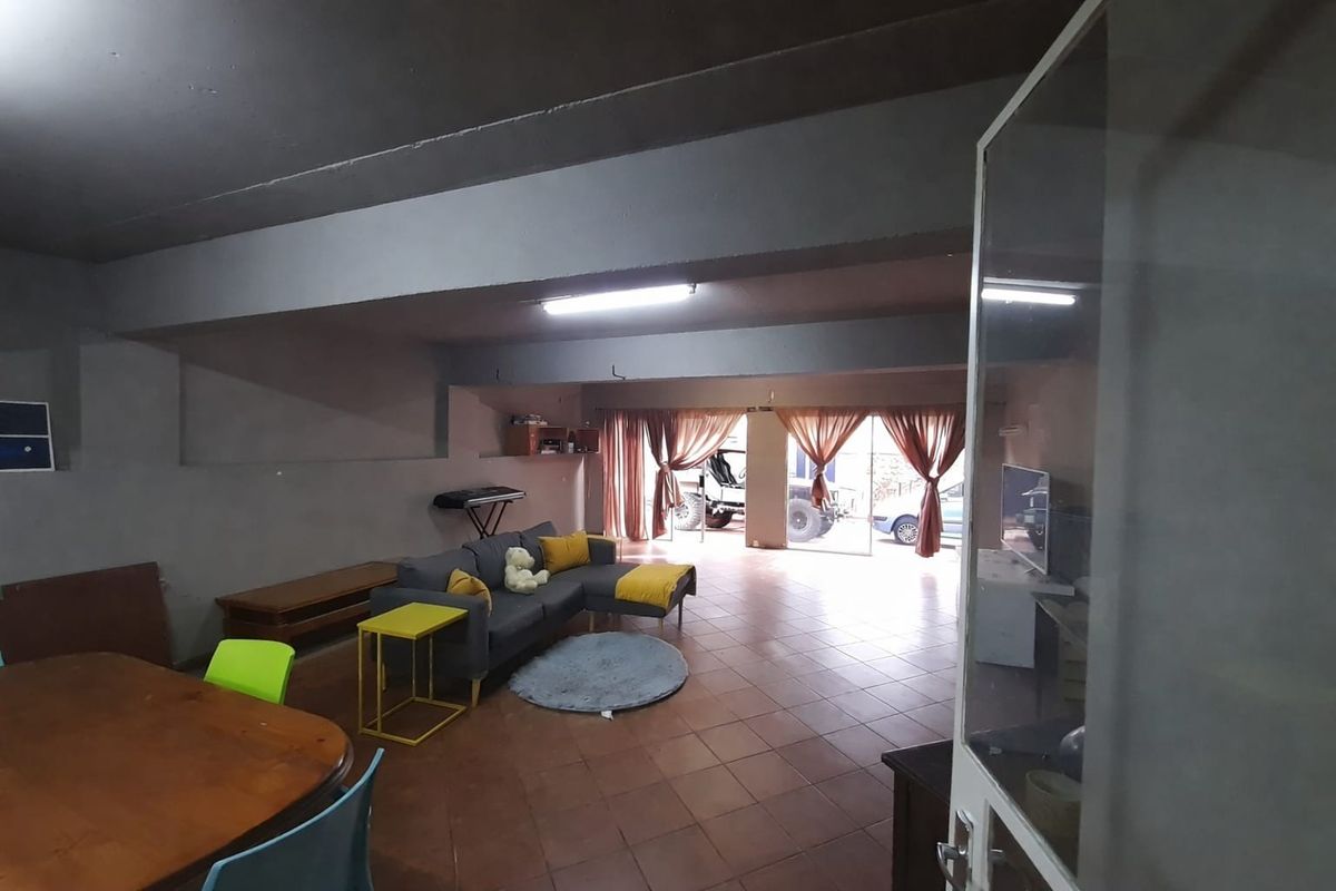 Spacious open-plan living area featuring tiled flooring and exposed concrete ceiling beams, with direct access to the exterior through sliding glass doors.