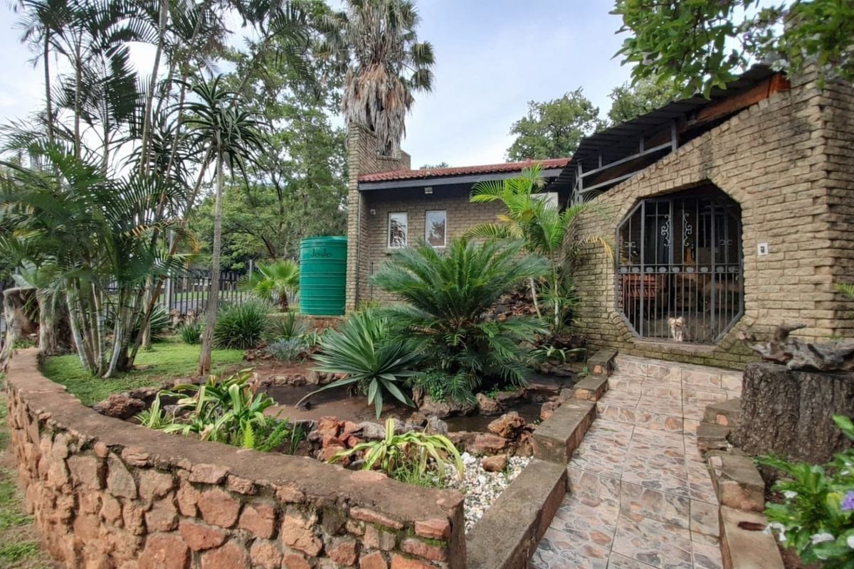 Rear exterior view featuring a face brick facade, stone retaining wall, landscaped garden, and a tiled walkway leading to a secure entrance.