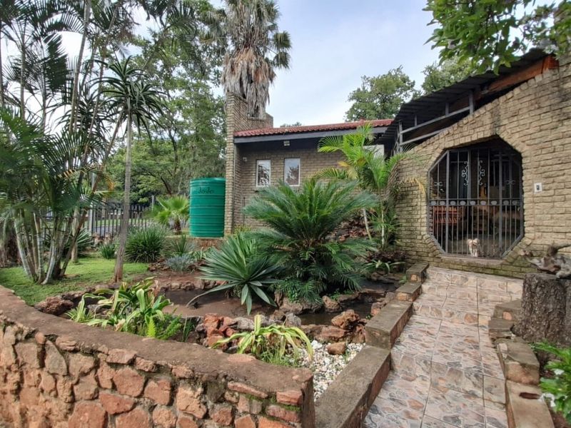 Rear exterior view featuring a face brick facade, stone retaining wall, landscaped garden, and a tiled walkway leading to a secure entrance.