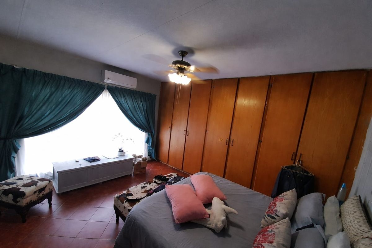 A bedroom featuring extensive built-in wooden cabinetry, a ceiling fan, wall-mounted air conditioning, and tiled flooring.