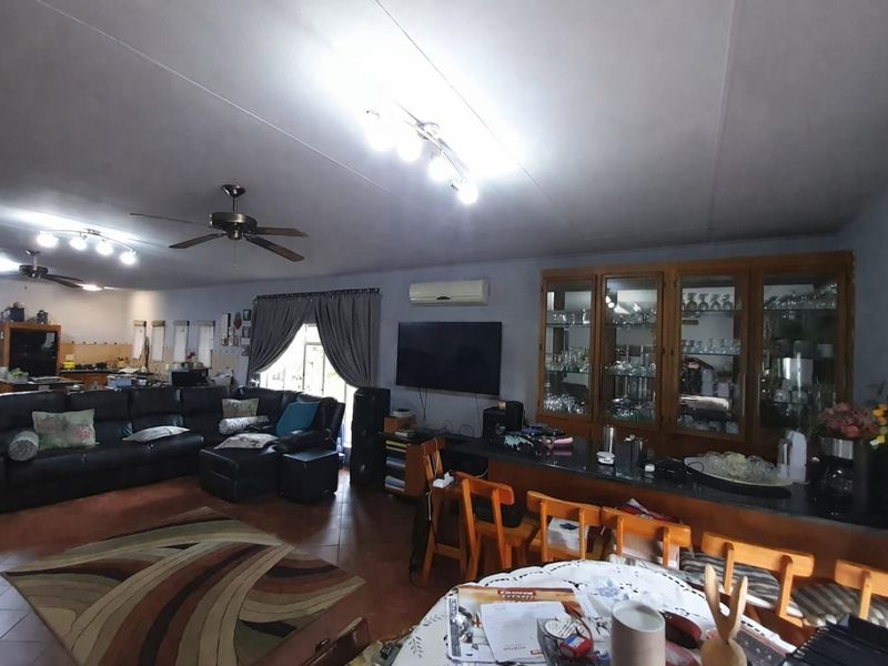 Spacious open-plan living area featuring tiled flooring, a built-in display cabinet, breakfast bar, and ceiling fans, providing a functional and versatile family space.