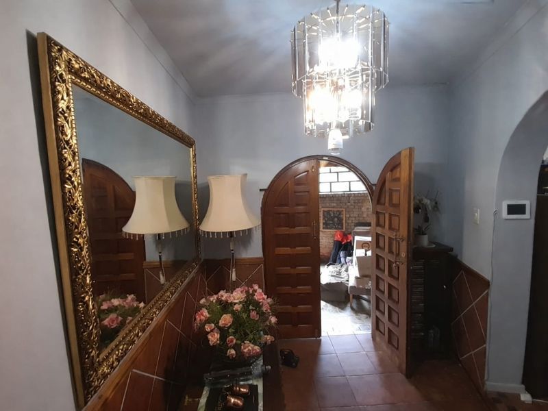 An inviting entryway featuring classic arched wooden double doors, decorative tiled wainscoting, and a prominent crystal chandelier, leading into the main living area.