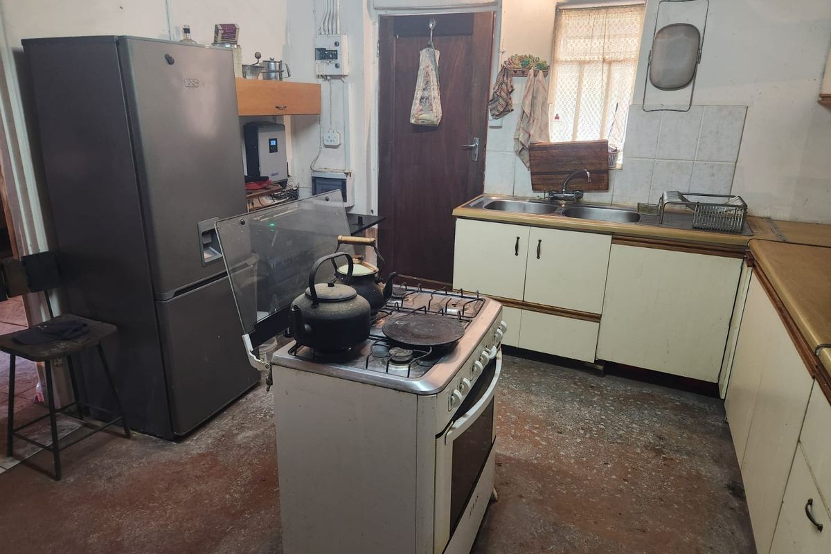 A dated kitchen featuring original cabinetry, a freestanding stove, and a double sink, requiring significant modernization and cosmetic updates to improve functionality and aesthetic appeal.